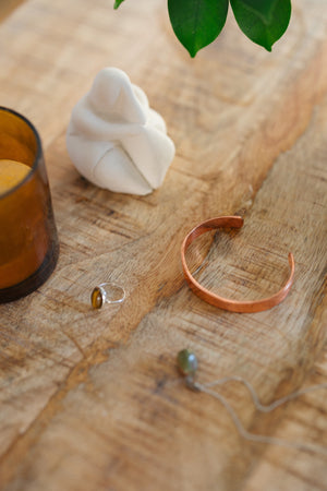 Kopero Copper Bracelet Smooth, on a wooden table next to a figurine and a ring