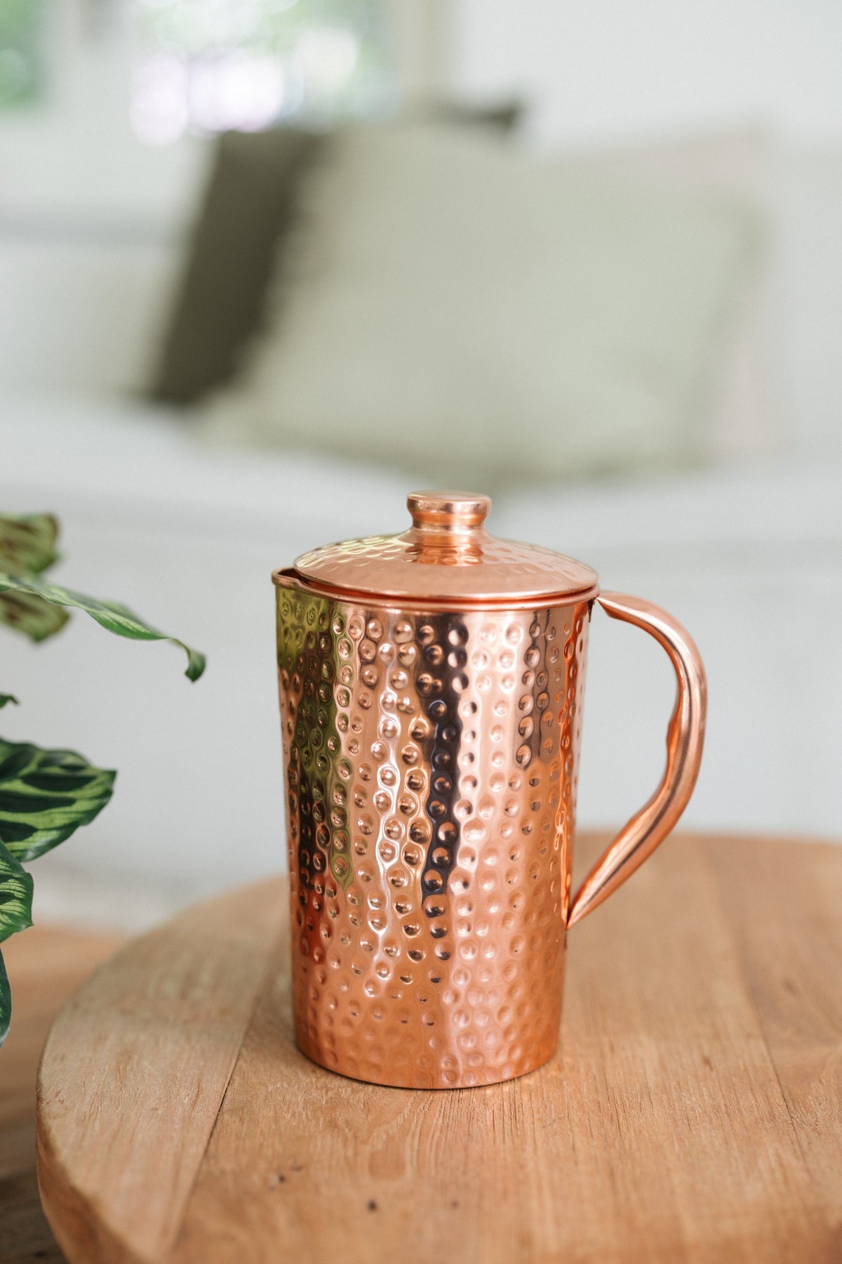 Kopero Copper Jug Hammered, on a round wooden table in front of a sofa