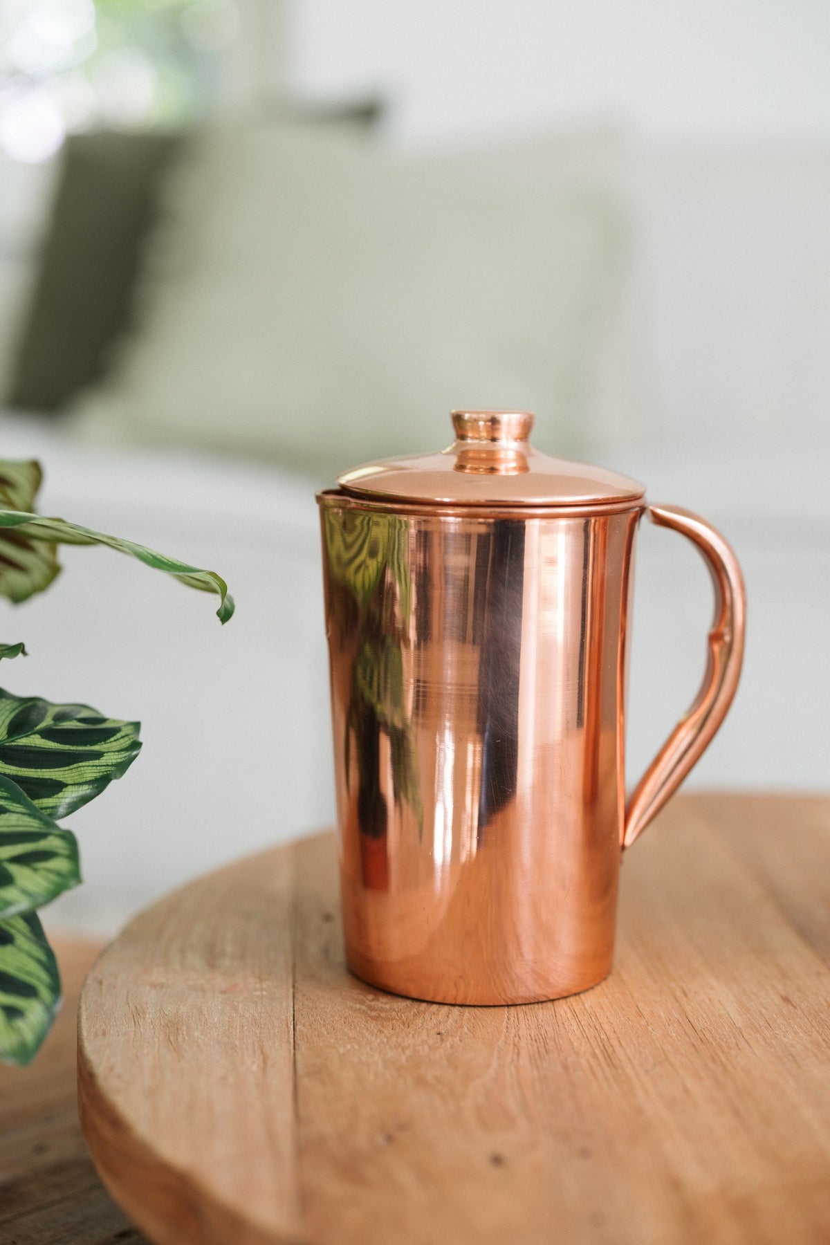 Kopero Copper Jug Smooth, on a round wooden table in front of a sofa