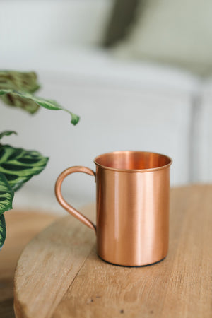 Kopero Copper Mug Smooth, on a round wooden table in front of a sofa