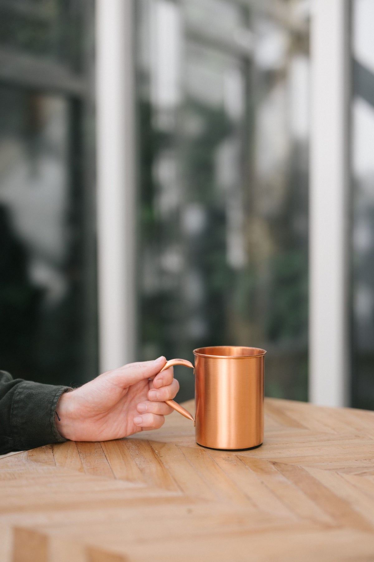 Kopero Copper Mug Smooth, on a wooden table, with a hand on the handle