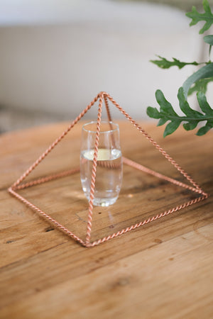 Kopero Copper Pyramid Energizer Twisted Large (23.56 cm), with a glass of water underneath