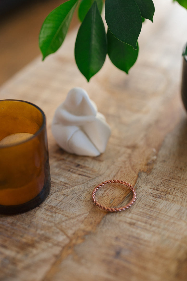 Kopero Copper Tensor Ring, on a wooden table next to a glass candle holder and a figurine